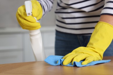 Photo of Woman using cleaning product while wiping wooden table with rag indoors, closeup