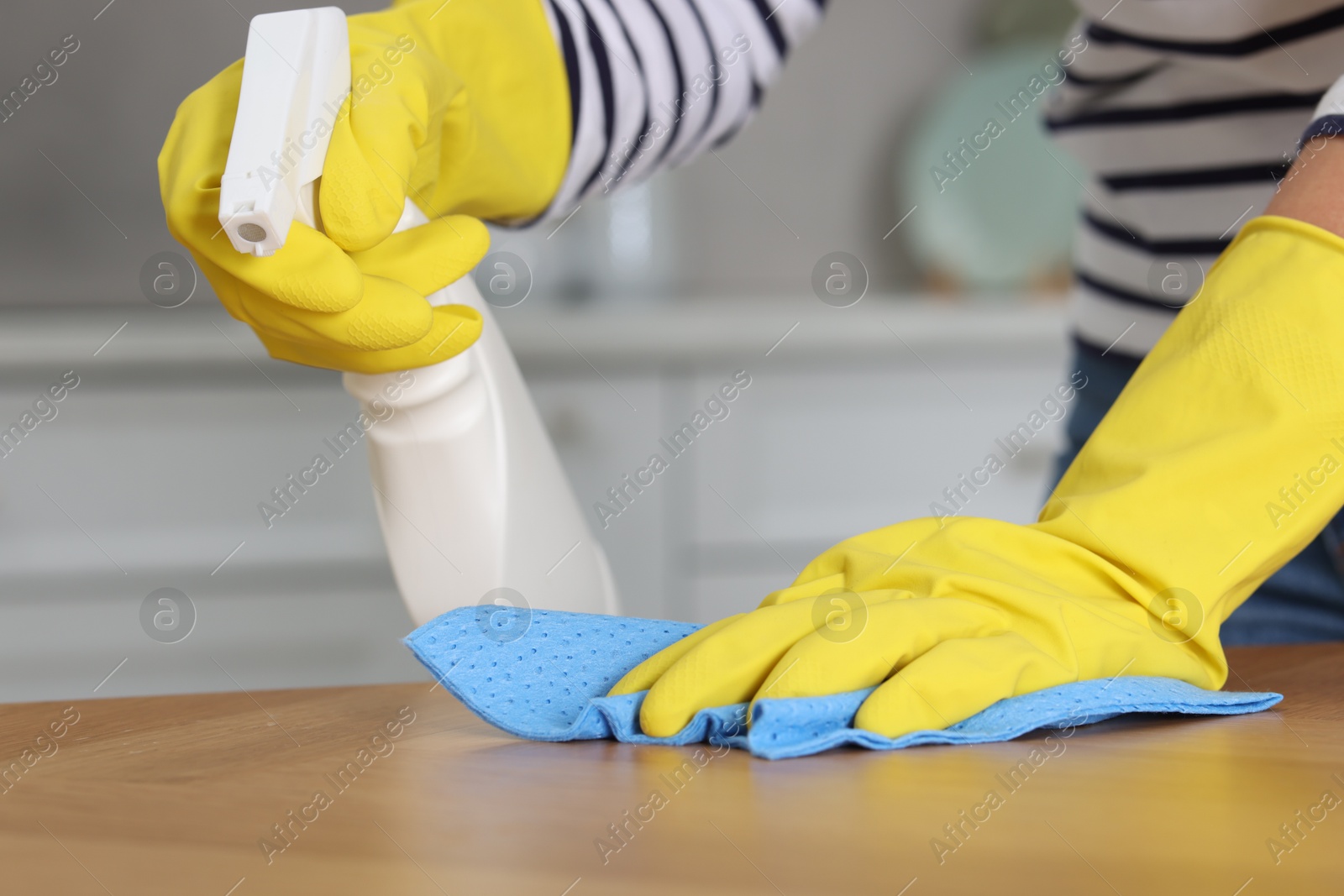 Photo of Woman using cleaning product while wiping wooden table with rag indoors, closeup