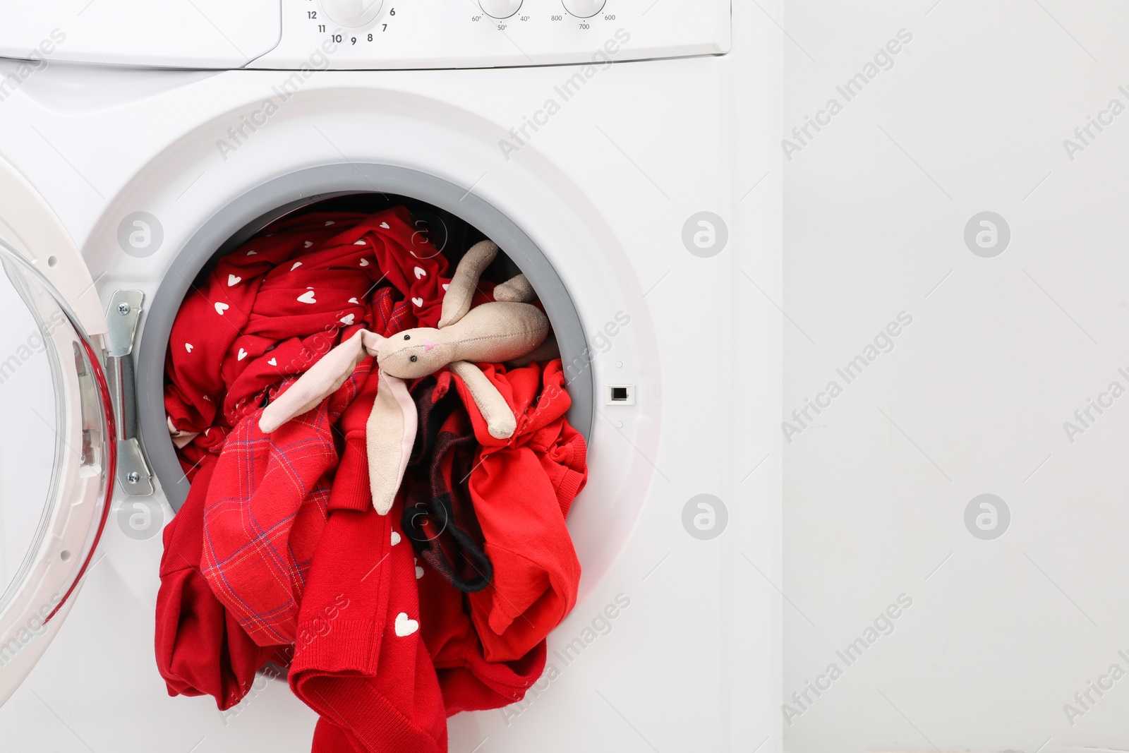 Photo of Washing machine with clothes and toy bunny near light wall, closeup