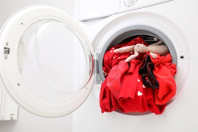 Photo of Washing machine with clothes and toy bunny indoors, closeup