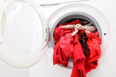 Photo of Washing machine with clothes and toy bunny as background, closeup