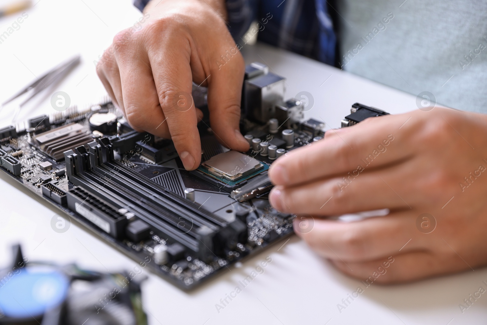 Photo of Man installing computer chip onto motherboard at white table, closeup