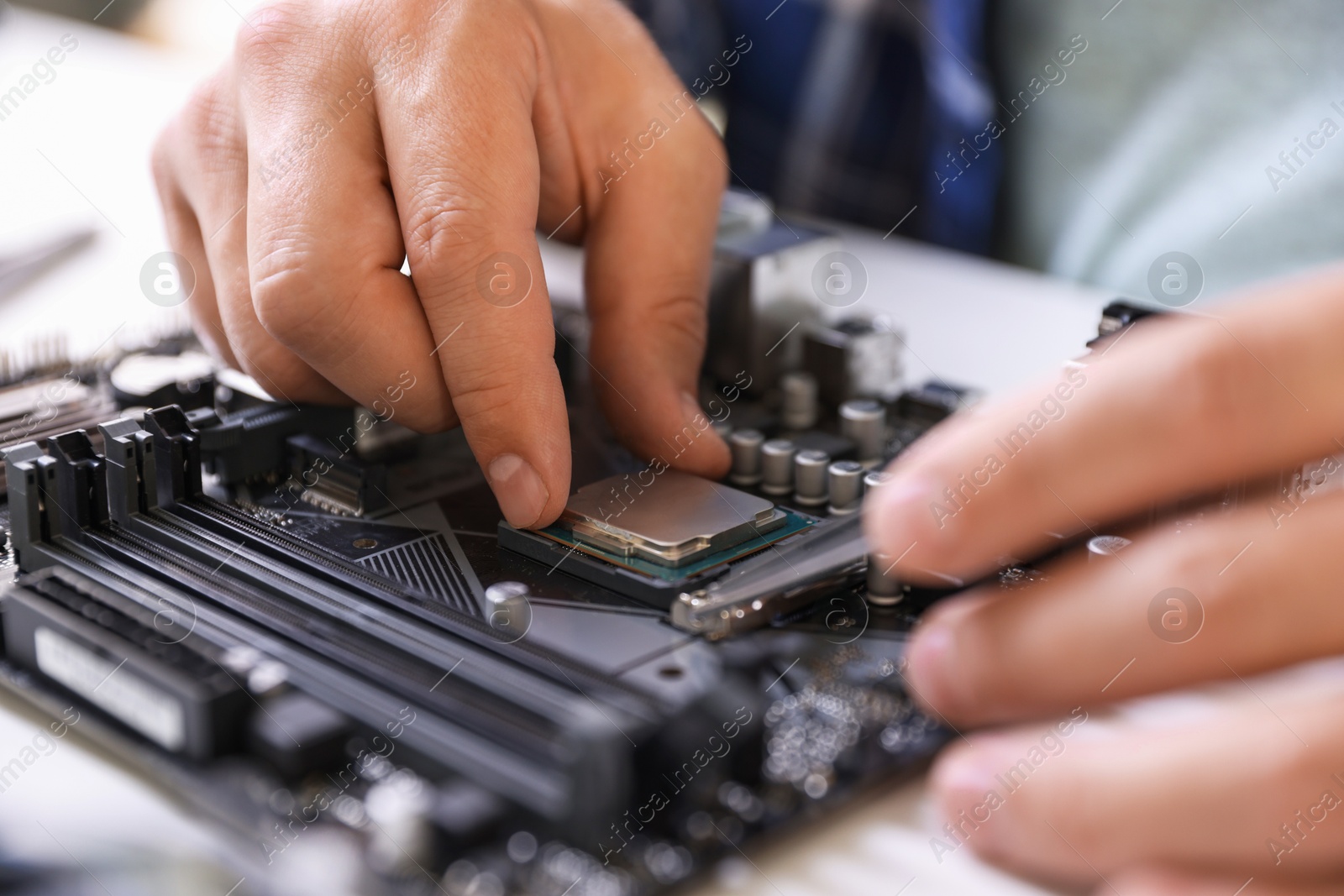 Photo of Man installing computer chip onto motherboard at white table, closeup