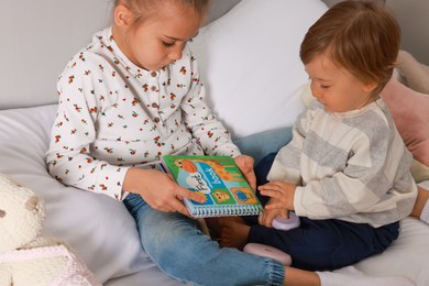 Photo of Sister and brother reading book together on bed indoors