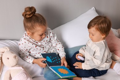 Photo of Sister and brother reading book together on bed indoors