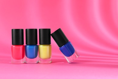 Photo of Nail polishes in bottles on pink background, space for text