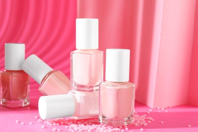 Photo of Nail polishes in bottles and beads on pink background