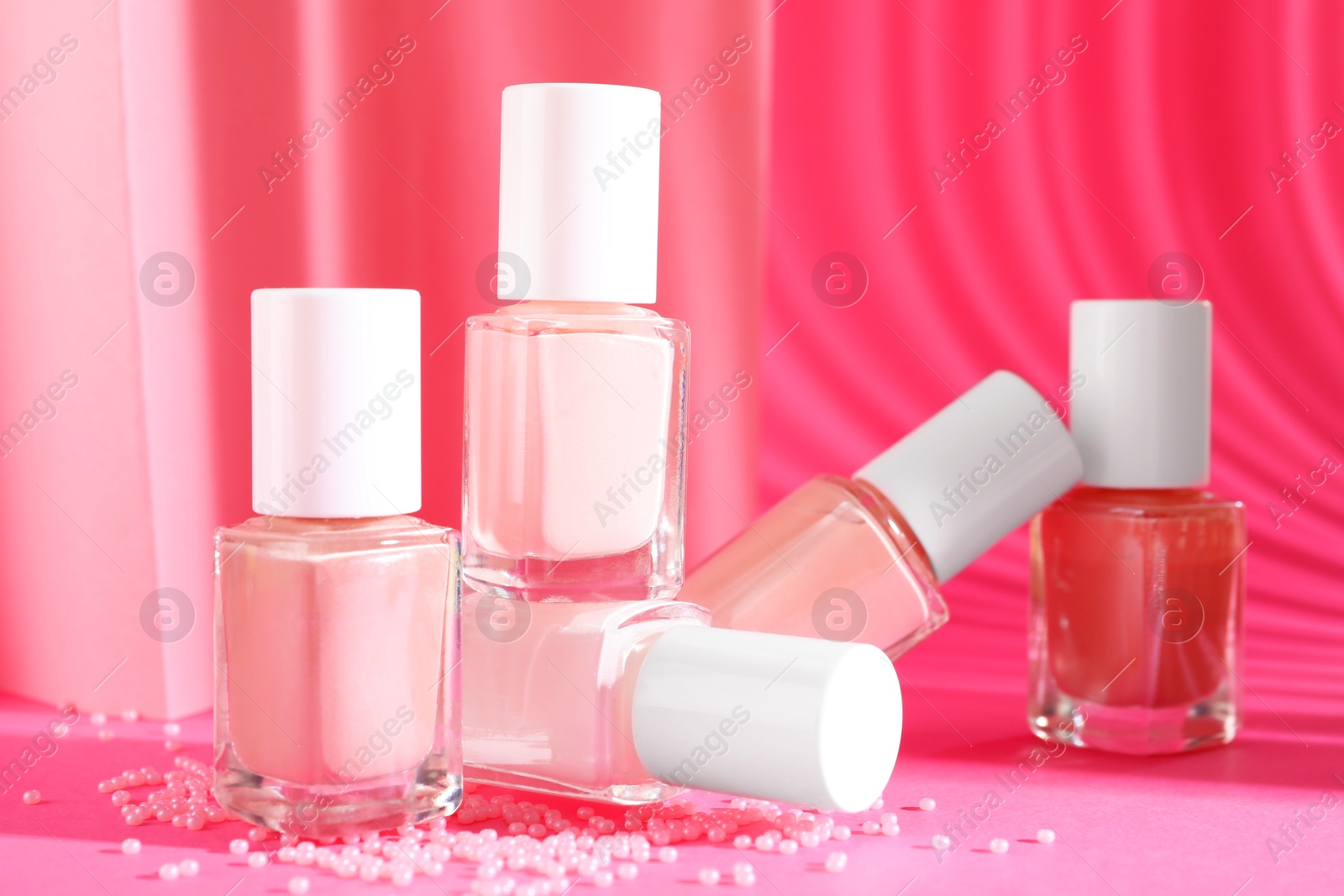 Photo of Nail polishes in bottles and beads on pink background