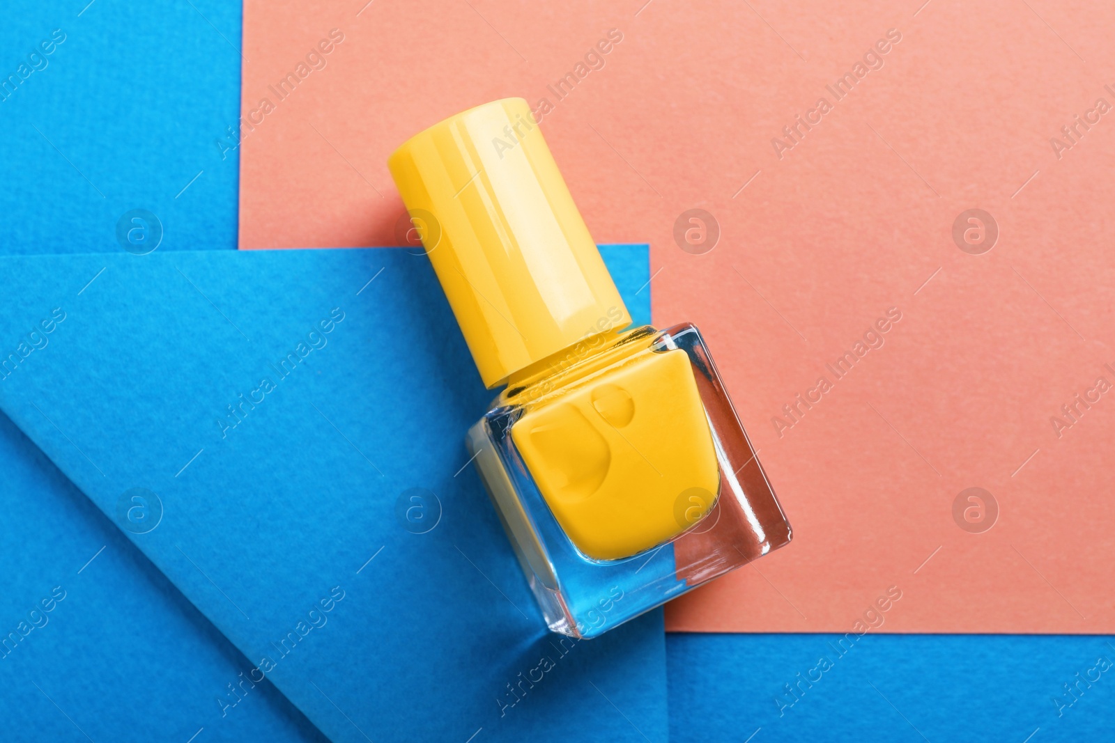 Photo of Nail polish in bottle on color background, top view