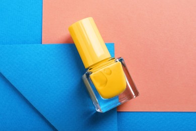 Photo of Nail polish in bottle on color background, top view