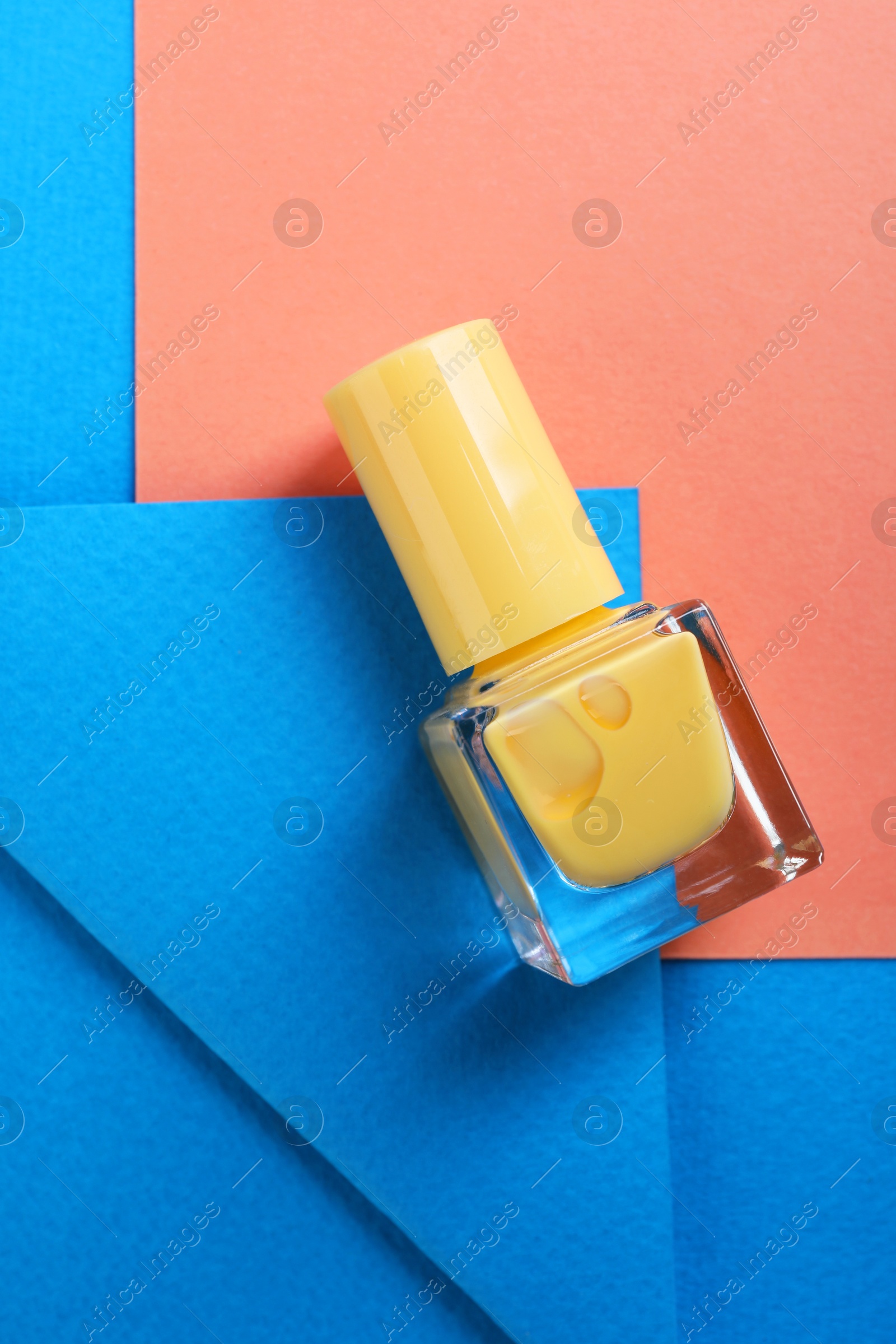 Photo of Nail polish in bottle on color background, top view