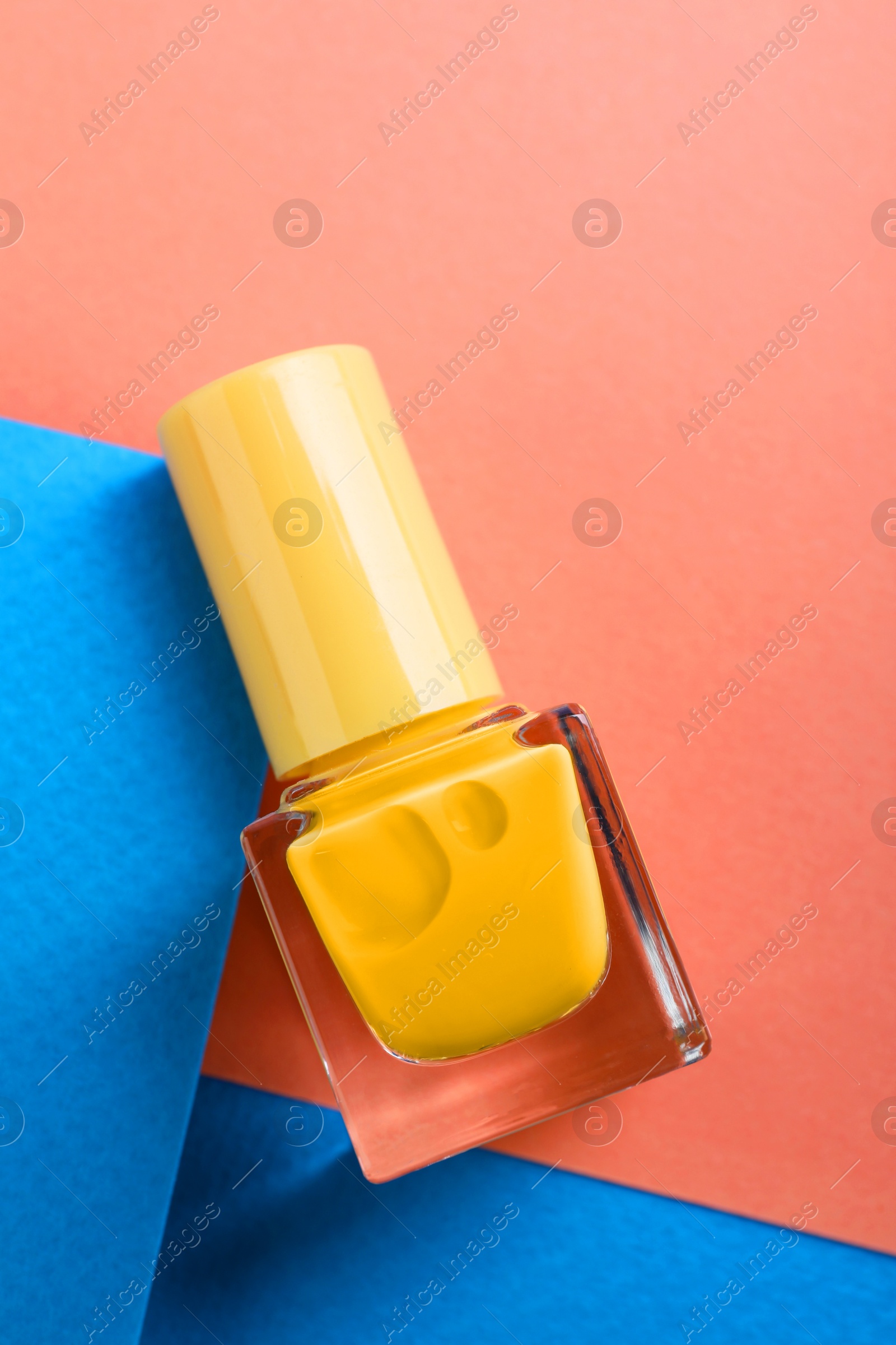 Photo of Nail polish in bottle on color background, top view