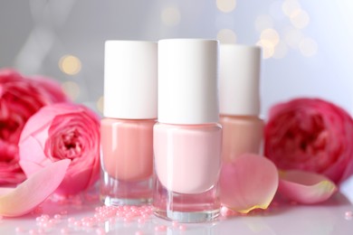 Photo of Nail polishes in bottles, beads and beautiful flowers on white table, closeup