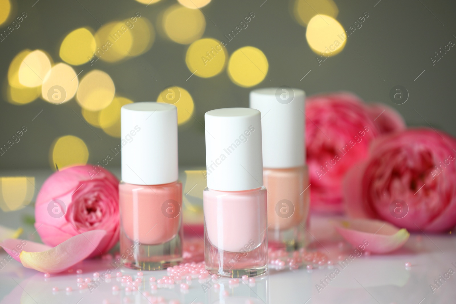 Photo of Nail polishes in bottles, beads and beautiful flowers on white table, closeup