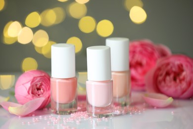 Photo of Nail polishes in bottles, beads and beautiful flowers on white table, closeup