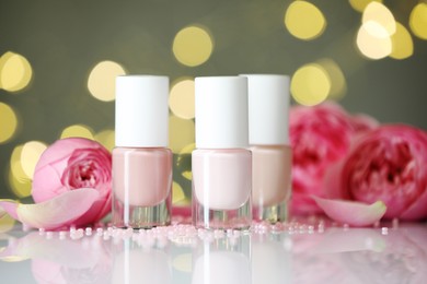 Photo of Nail polishes in bottles, beads and beautiful flowers on white table, closeup