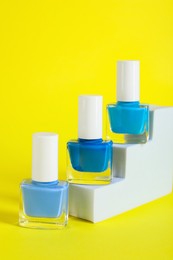 Photo of Stylish presentation of nail polishes in bottles on yellow background