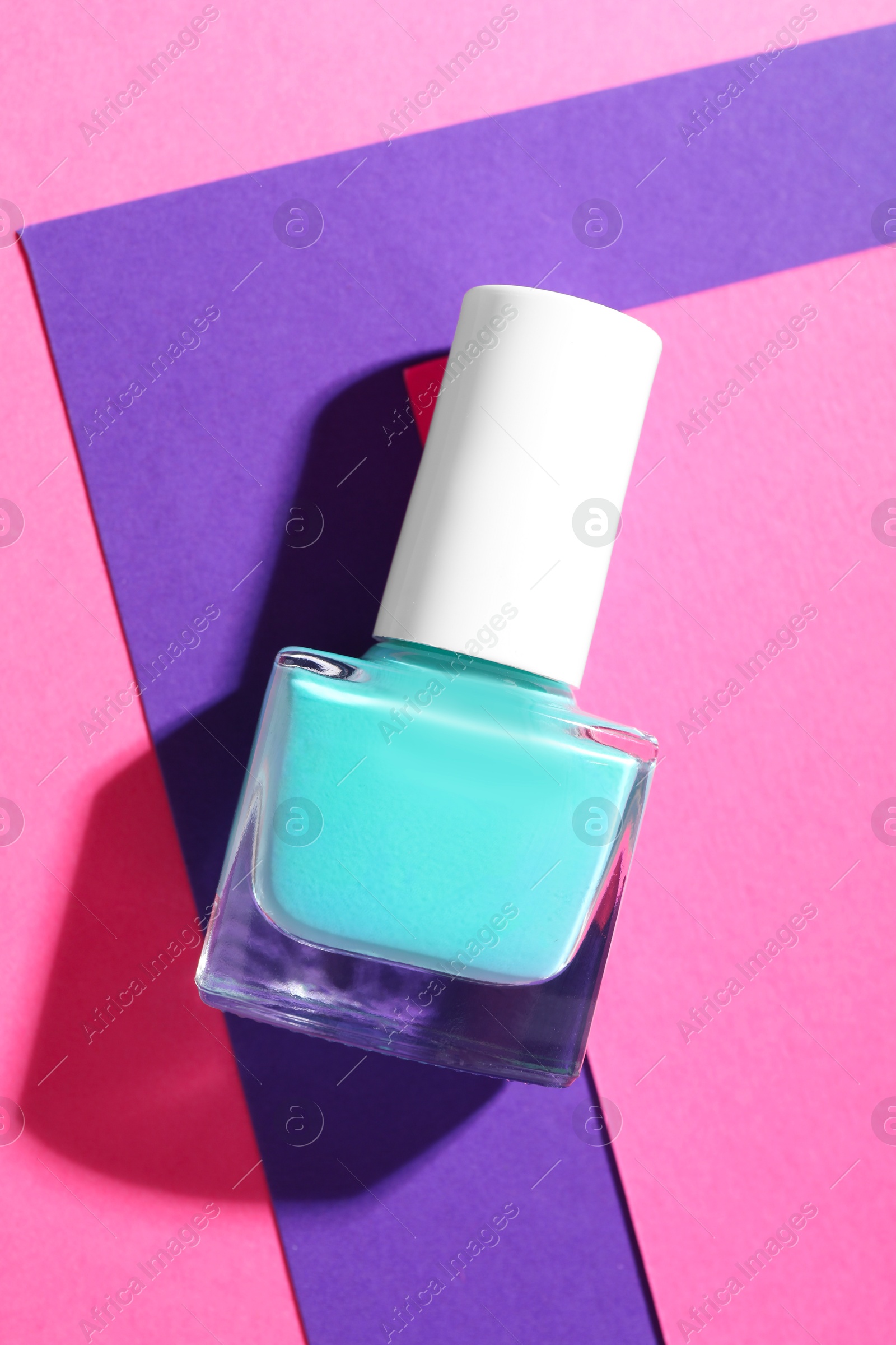 Photo of Nail polish in bottle on color background, top view