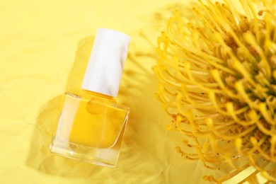 Photo of Nail polish in bottle and flower on yellow background, top view