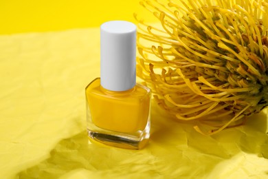 Photo of Nail polish in bottle and flower on yellow background, closeup