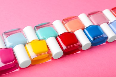 Photo of Set of different nail polishes in bottles on pink background, closeup