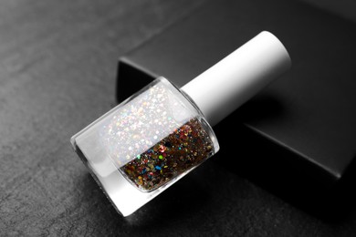 Photo of Glitter nail polish in bottle on dark textured table, closeup