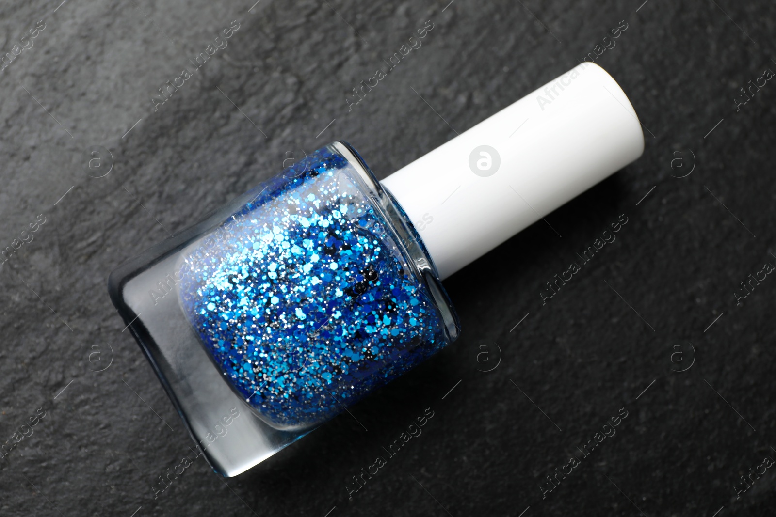 Photo of Glitter nail polish in bottle on dark textured table, top view