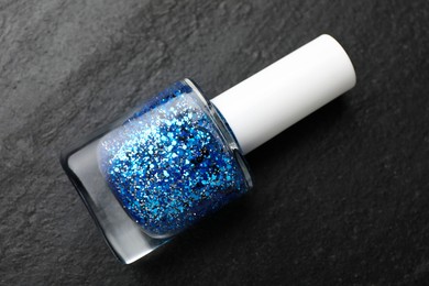 Photo of Glitter nail polish in bottle on dark textured table, top view