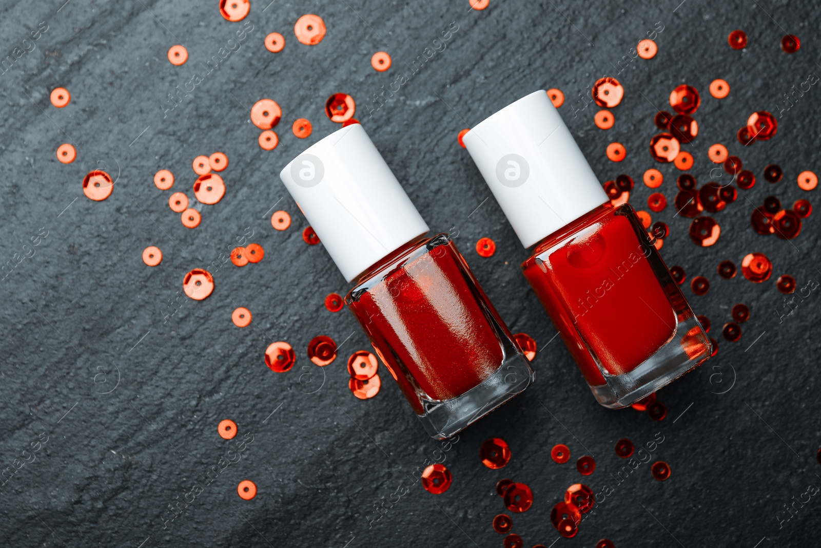 Photo of Red nail polishes in bottles on dark textured table, flat lay