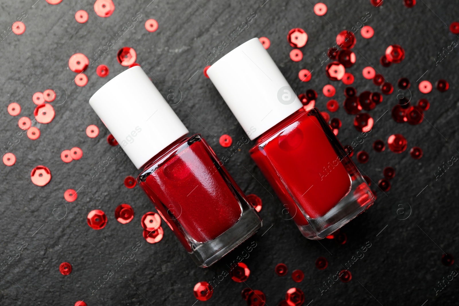 Photo of Red nail polishes in bottles on dark textured table, flat lay