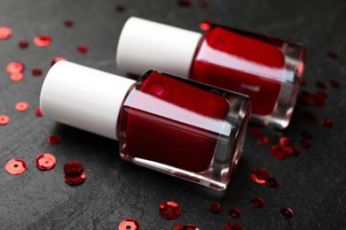 Photo of Red nail polishes in bottles on dark textured table, closeup