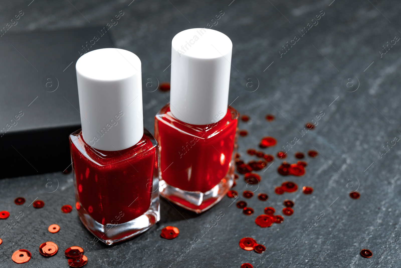 Photo of Red nail polishes in bottles on dark textured table, closeup. Space for text