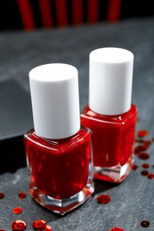 Photo of Red nail polishes in bottles on dark textured table, closeup