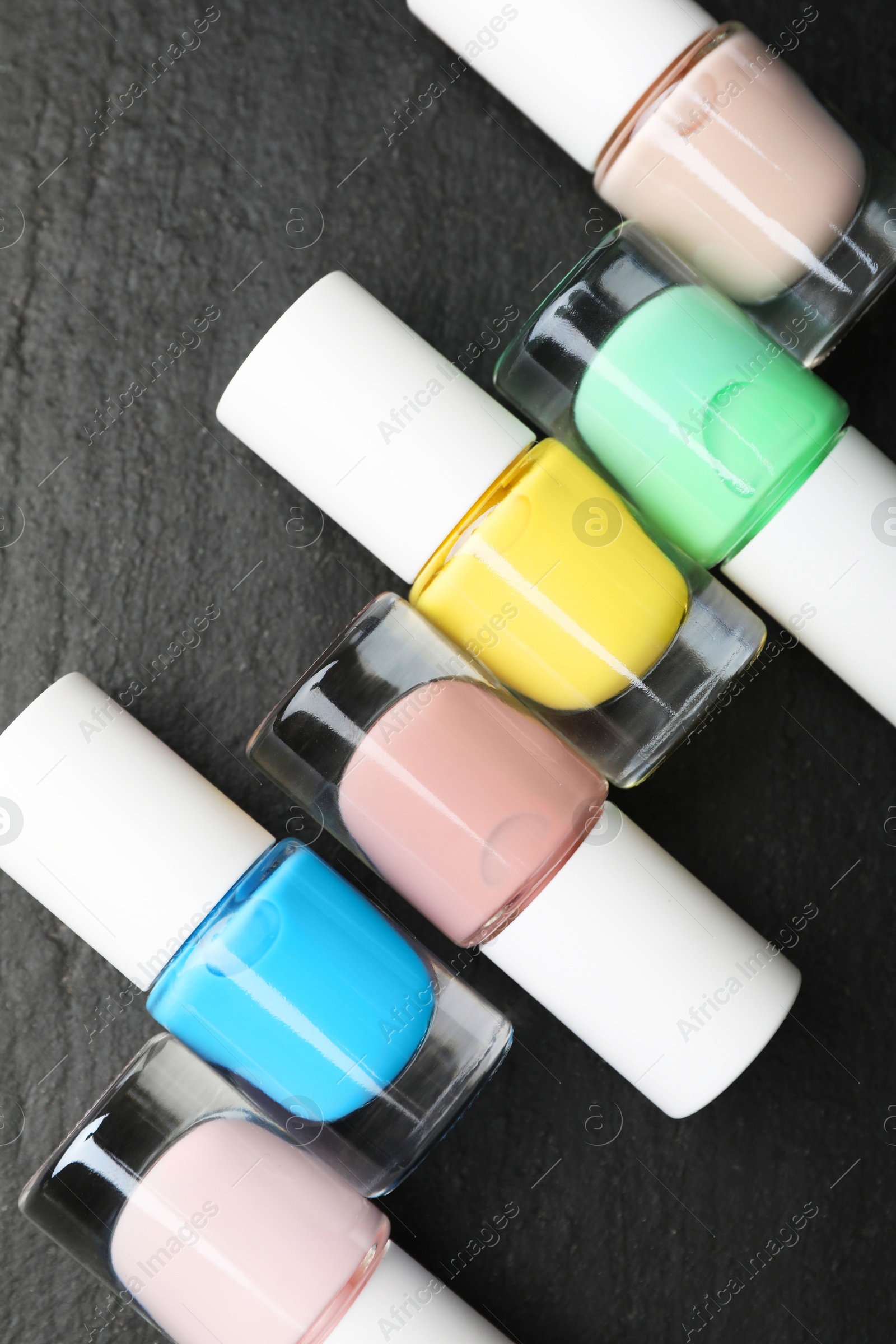 Photo of Set of different nail polishes in bottles on dark textured table, flat lay