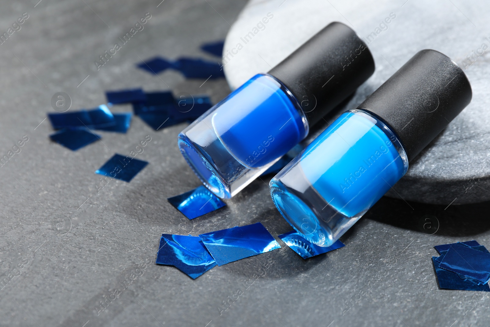 Photo of Stylish presentation of blue nail polishes in bottles on grey textured table, closeup. Space for text