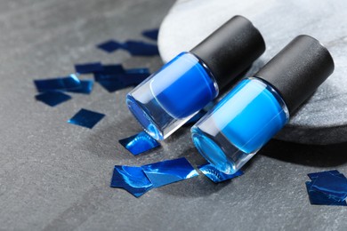 Photo of Stylish presentation of blue nail polishes in bottles on grey textured table, closeup. Space for text