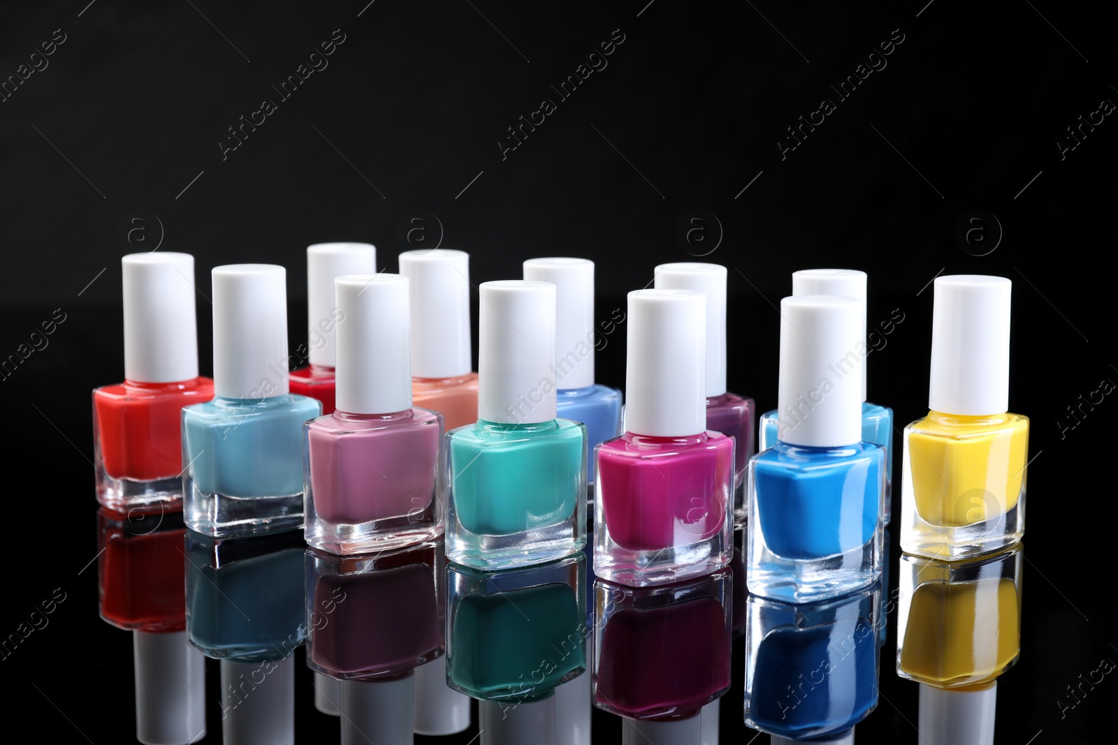 Photo of Set of different nail polishes in bottles on black mirror surface