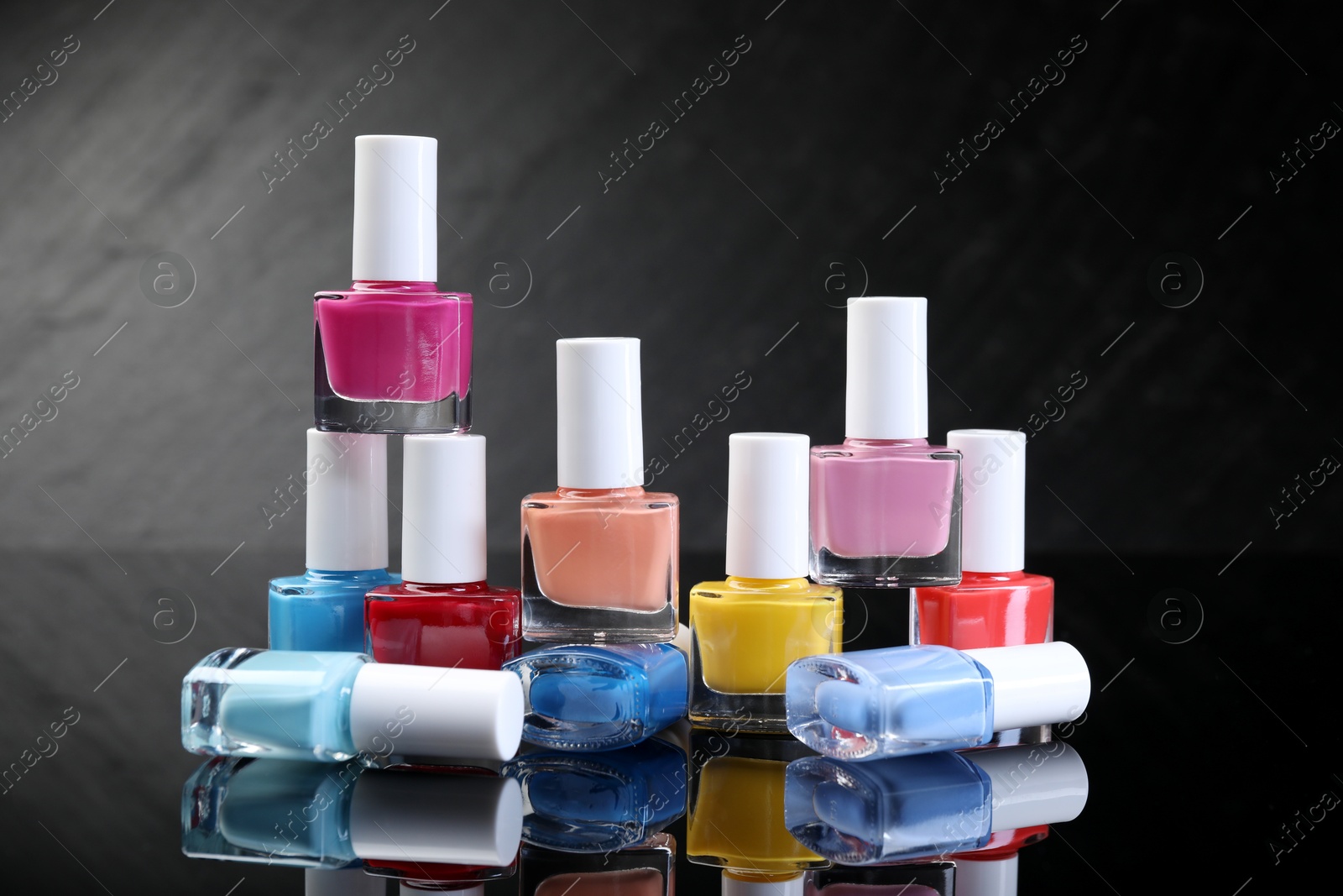 Photo of Set of different nail polishes in bottles on black mirror surface