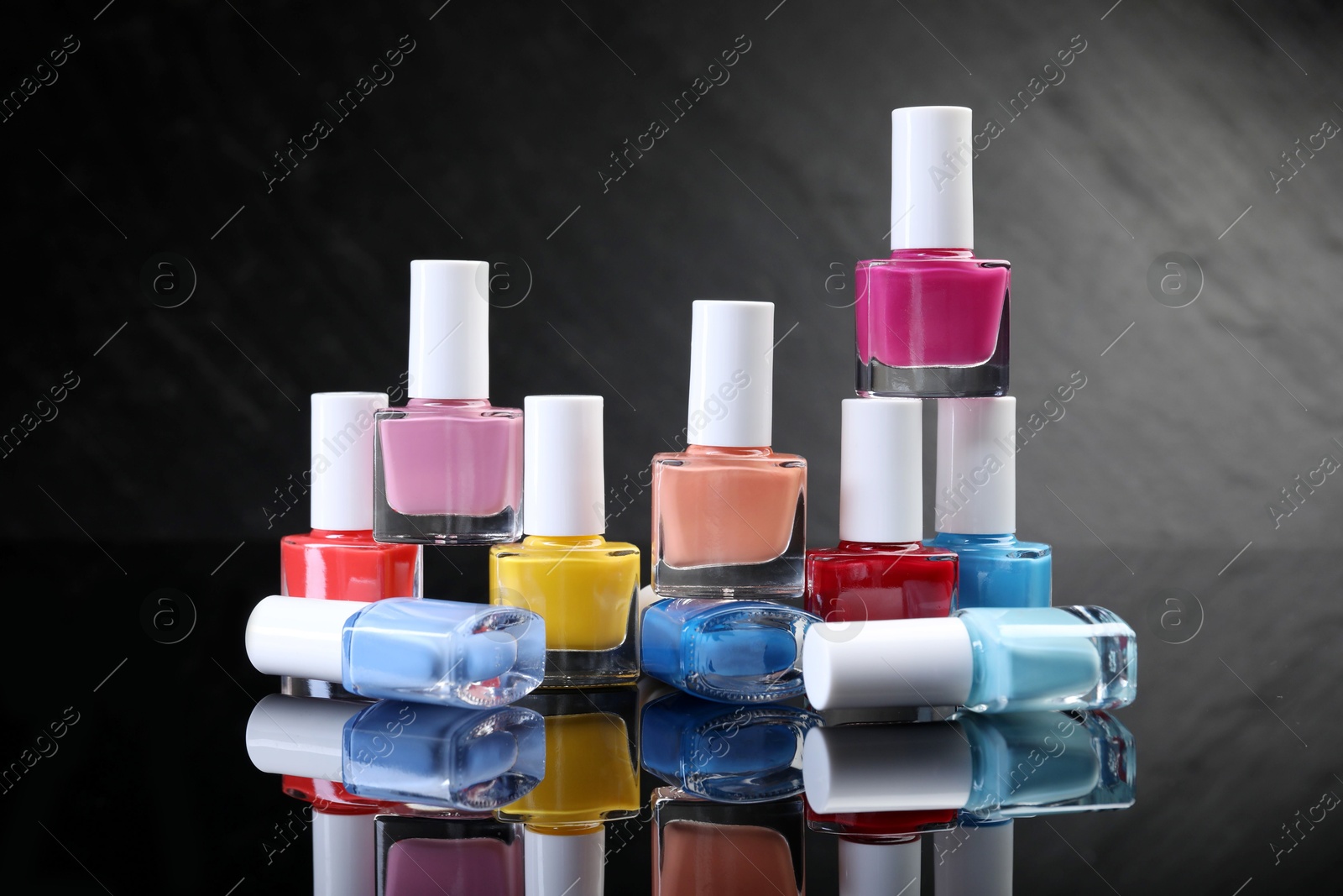 Photo of Set of different nail polishes in bottles on black mirror surface