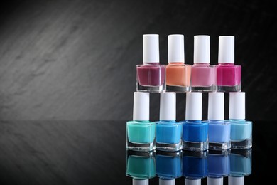 Photo of Set of different nail polishes in bottles on black mirror surface. Space for text