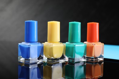 Photo of Set of different nail polishes in bottles on black mirror surface, closeup