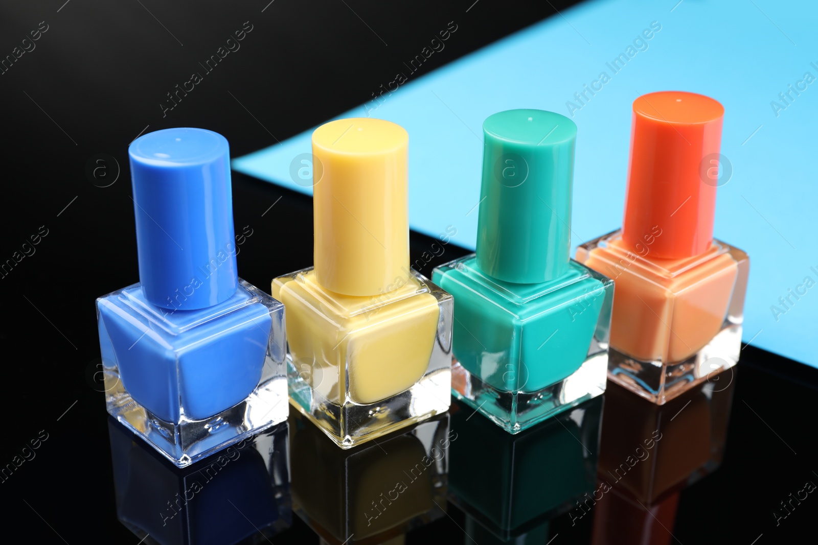 Photo of Set of different nail polishes in bottles on black mirror surface, closeup