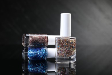 Photo of Set of glitter nail polishes in bottles on black mirror surface, closeup