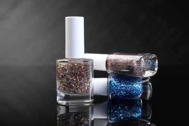 Photo of Set of glitter nail polishes in bottles on black mirror surface, closeup