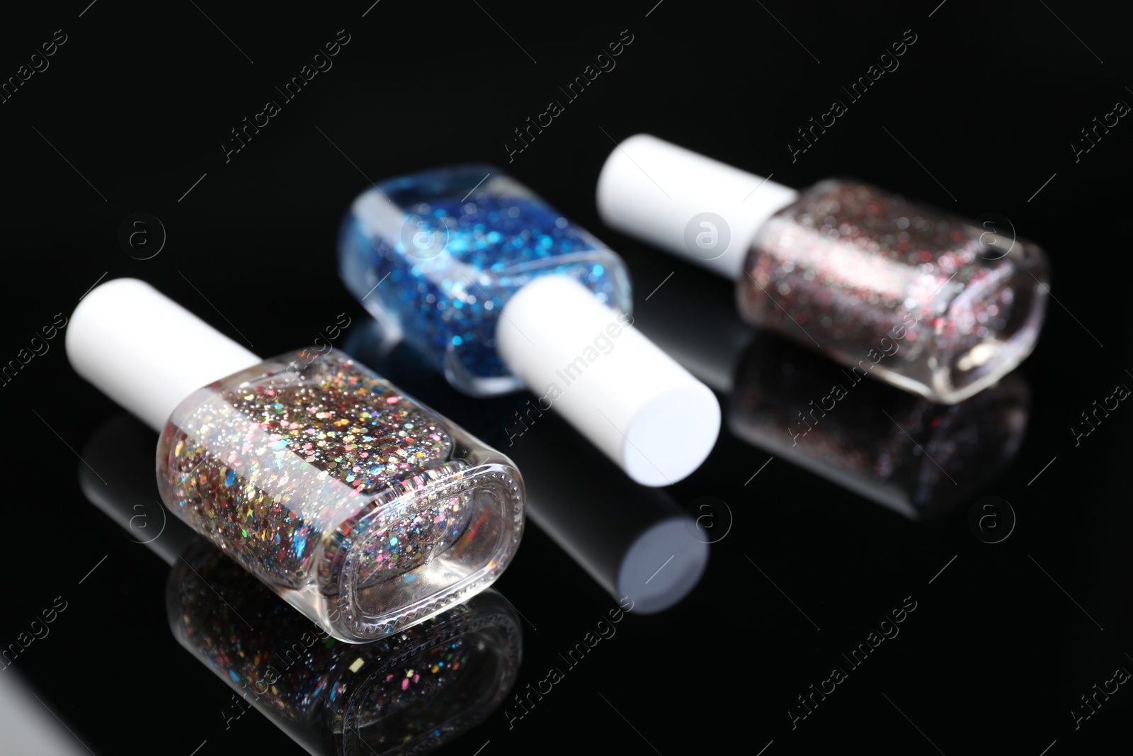 Photo of Set of glitter nail polishes in bottles on black mirror surface, closeup