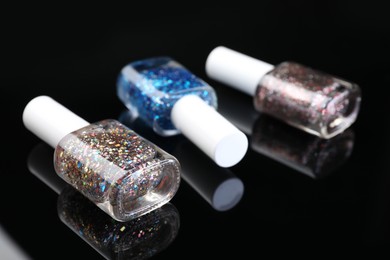 Photo of Set of glitter nail polishes in bottles on black mirror surface, closeup