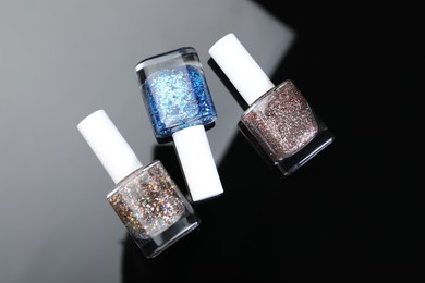 Photo of Set of glitter nail polishes in bottles on mirror surface, flat lay