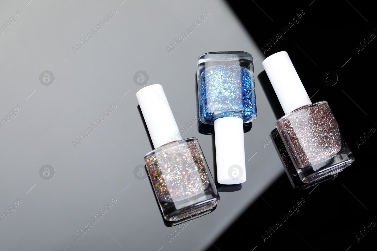 Photo of Set of glitter nail polishes in bottles on mirror surface, flat lay. Space for text