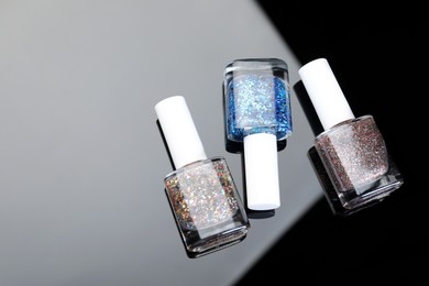 Photo of Set of glitter nail polishes in bottles on mirror surface, flat lay. Space for text