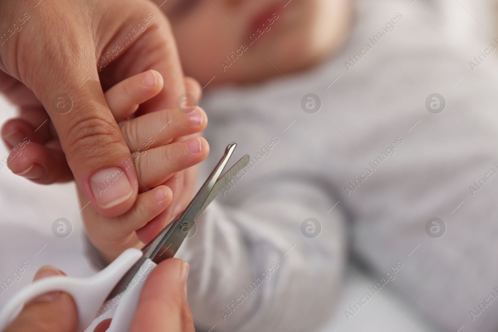 Photo of Mother cutting her cute little baby's nails on bed, closeup